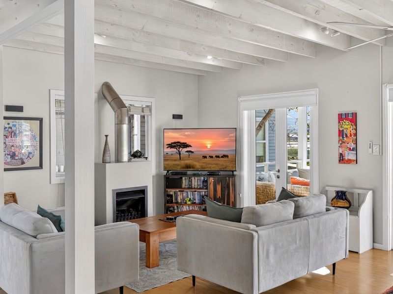 Bright living room featuring exposed timber beam ceilings, a built-in fireplace with a metal flue, and direct access to an outdoor patio area.