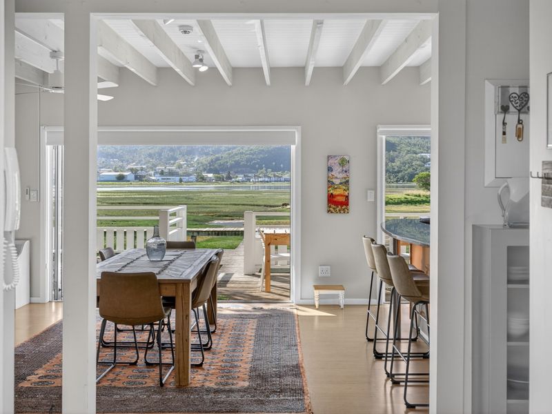Open-plan living and dining area featuring exposed white timber beams, light flooring, and large sliding doors opening to a scenic outdoor deck.