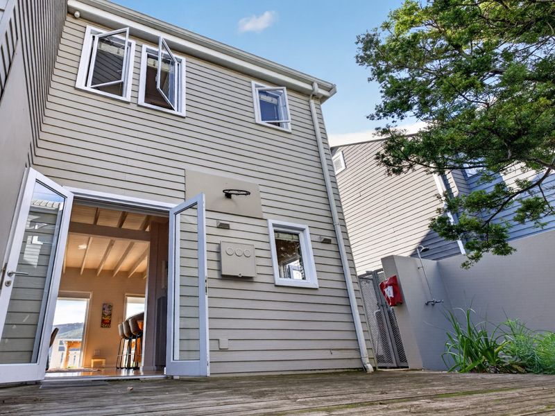 Rear exterior view featuring timber decking, weatherboard cladding, double-door access to the interior, and an outdoor shower area.