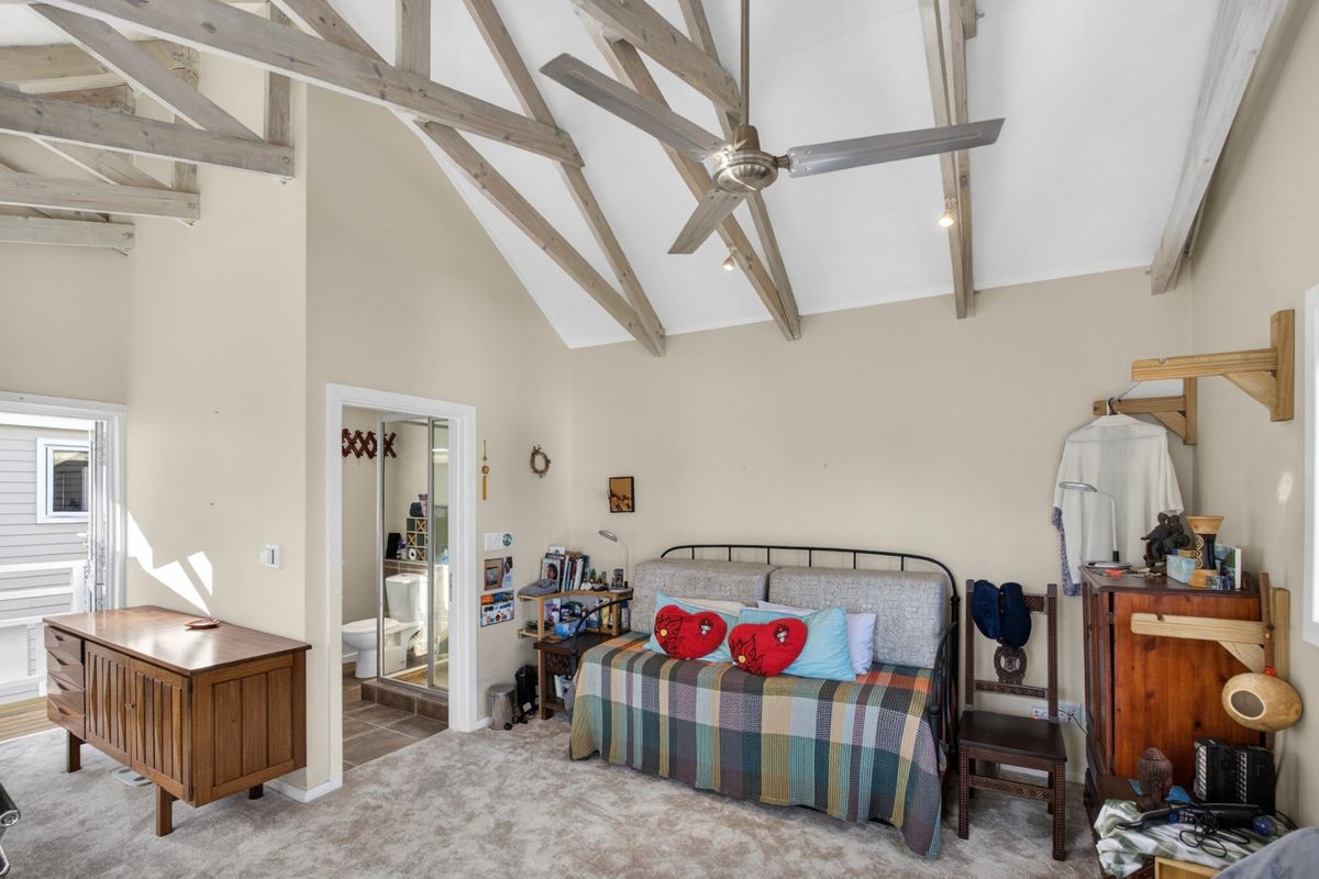 A bedroom featuring high vaulted ceilings with exposed timber trusses, a ceiling fan, and an en-suite bathroom.