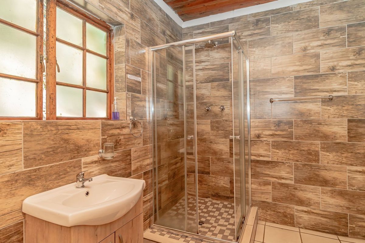 A well-maintained bathroom featuring wood-look wall tiling, a glass shower enclosure, and a vanity basin with a timber-style cabinet.
