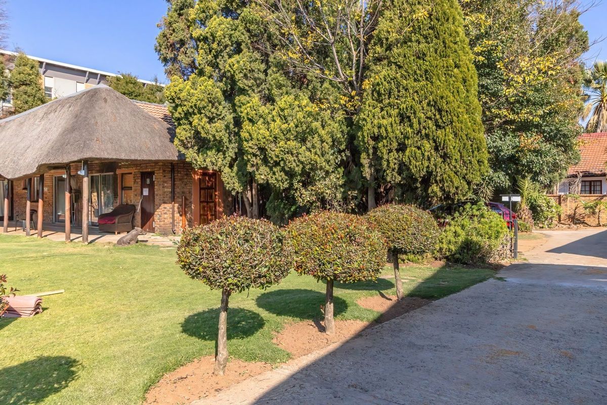 Rear view of a commercial property featuring a thatched roof building, paved driveway, and well-maintained garden area.