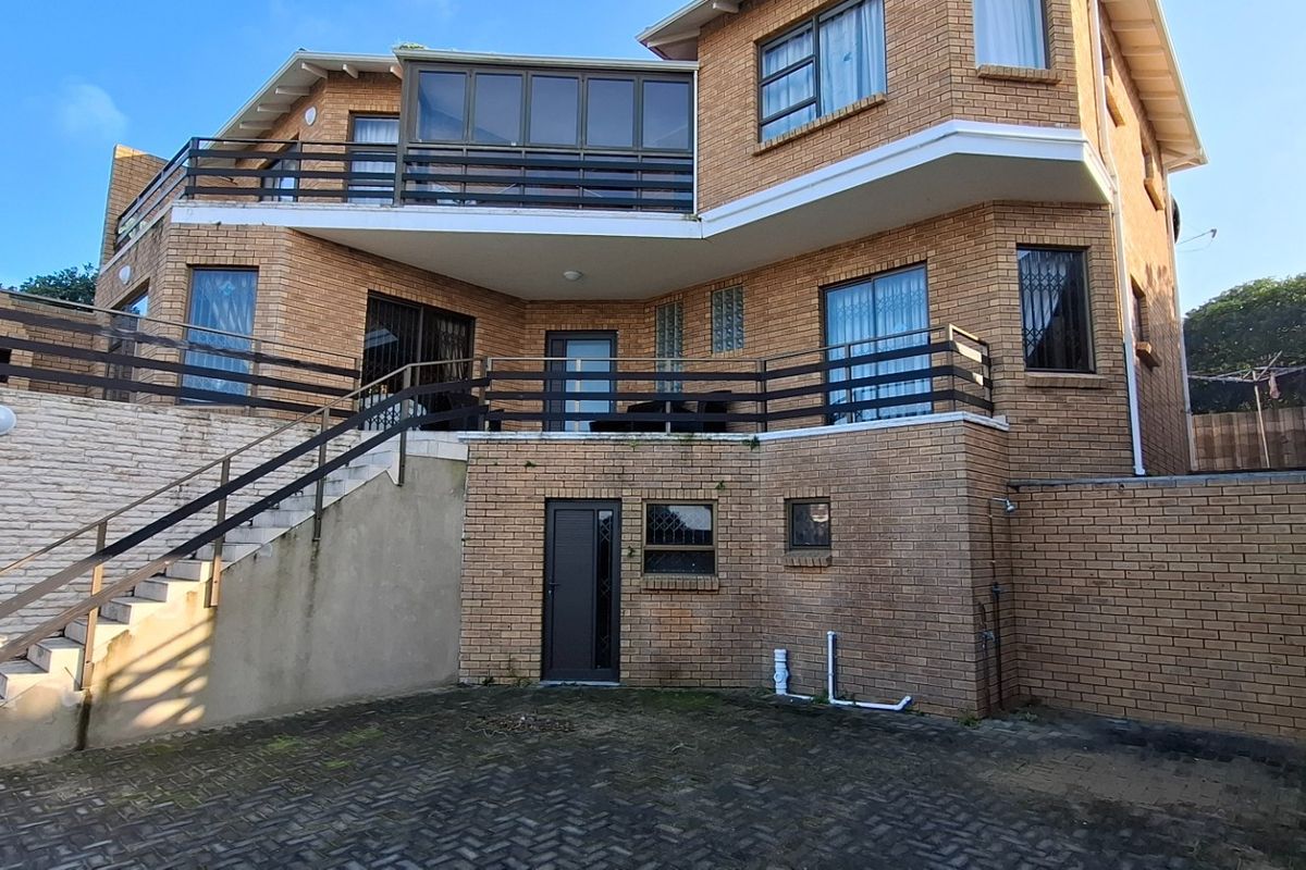 Rear view of a multi-level brick house featuring a large balcony, external staircase, and paved courtyard area.