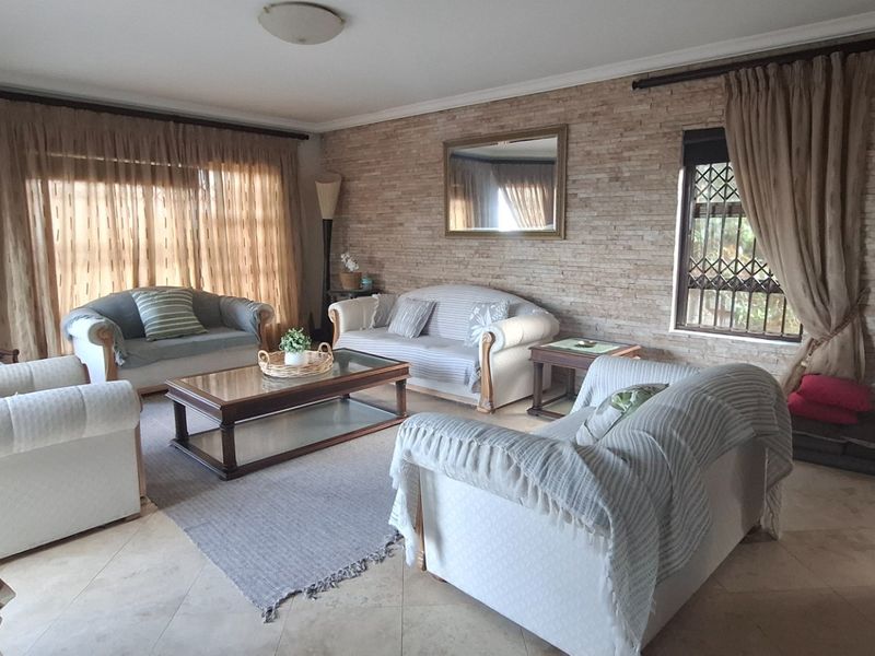 Spacious living room featuring a textured stone feature wall, large windows with natural light, and neutral tiled flooring.