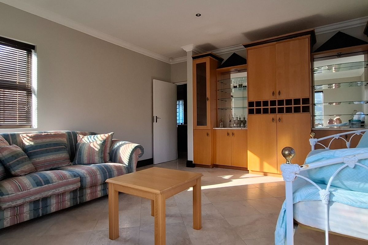 A spacious bedroom featuring tiled flooring, built-in wooden cabinetry, and large windows with fitted blinds, offering a functional and well-lit living space.