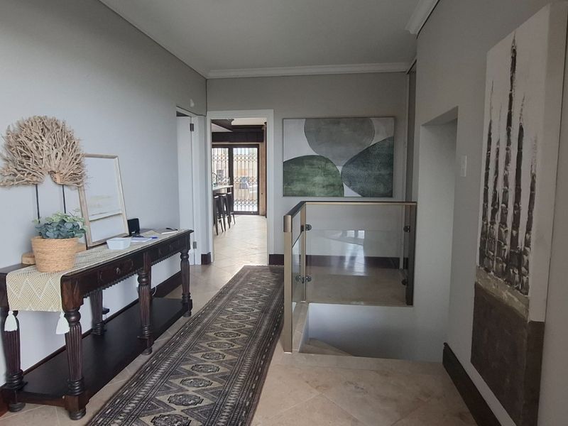 A bright and welcoming entrance hallway featuring tiled flooring and a modern glass balustrade overlooking the staircase.
