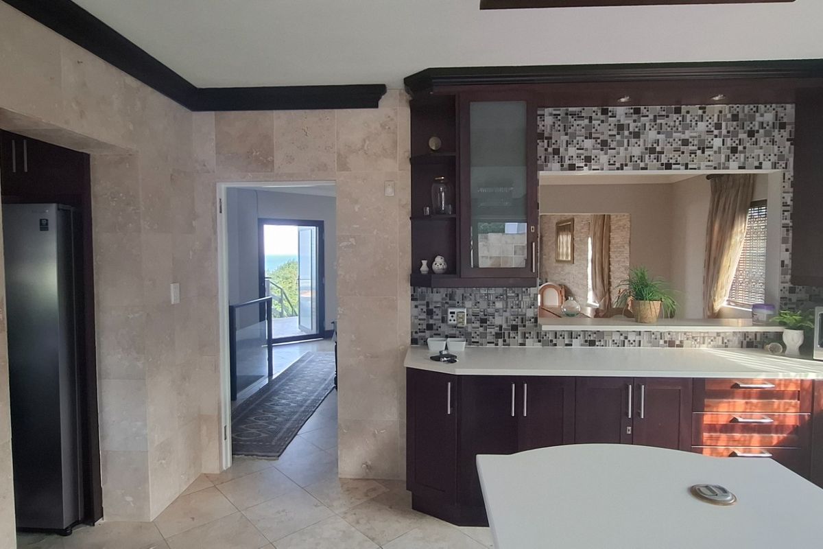A well-appointed kitchen featuring dark wood cabinetry, stone tile wall cladding, mosaic backsplash, and a breakfast counter, with an adjacent doorway leading to a balcony.