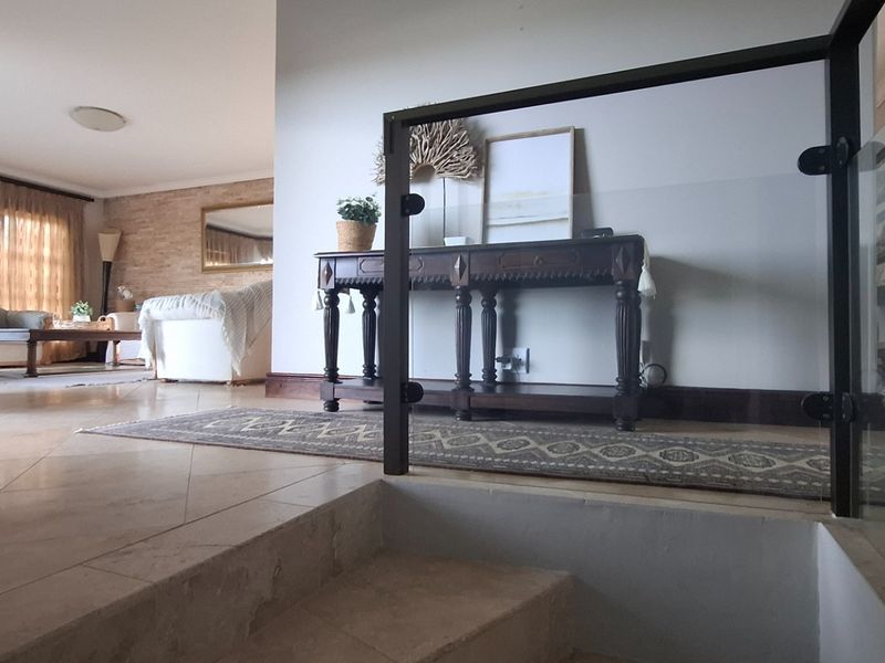 A view from a staircase landing looking into an open-plan living area, featuring tiled flooring and a modern glass balustrade.
