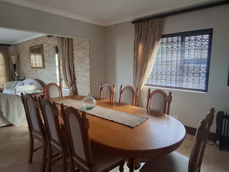 Open plan dining and living area featuring tiled flooring, a textured stone feature wall, and large windows with fitted blinds.