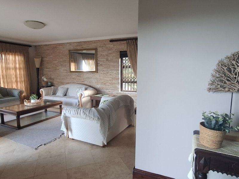 A comfortable living room featuring a textured stone feature wall, tiled flooring, and large windows with curtains, creating a warm and inviting atmosphere.