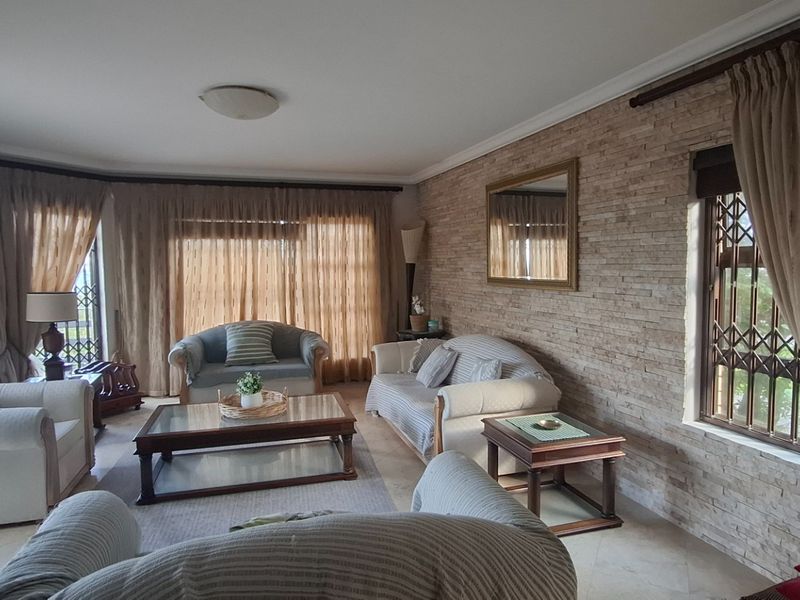 Spacious living room featuring a textured stone feature wall, tiled flooring, and large windows secured with metal security gates.