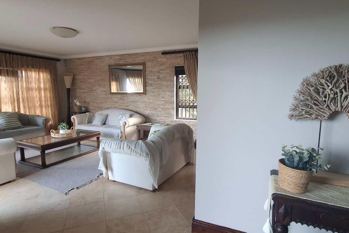 A comfortable living room featuring a textured stone feature wall, tiled flooring, and large windows with curtains, creating a warm and inviting atmosphere.