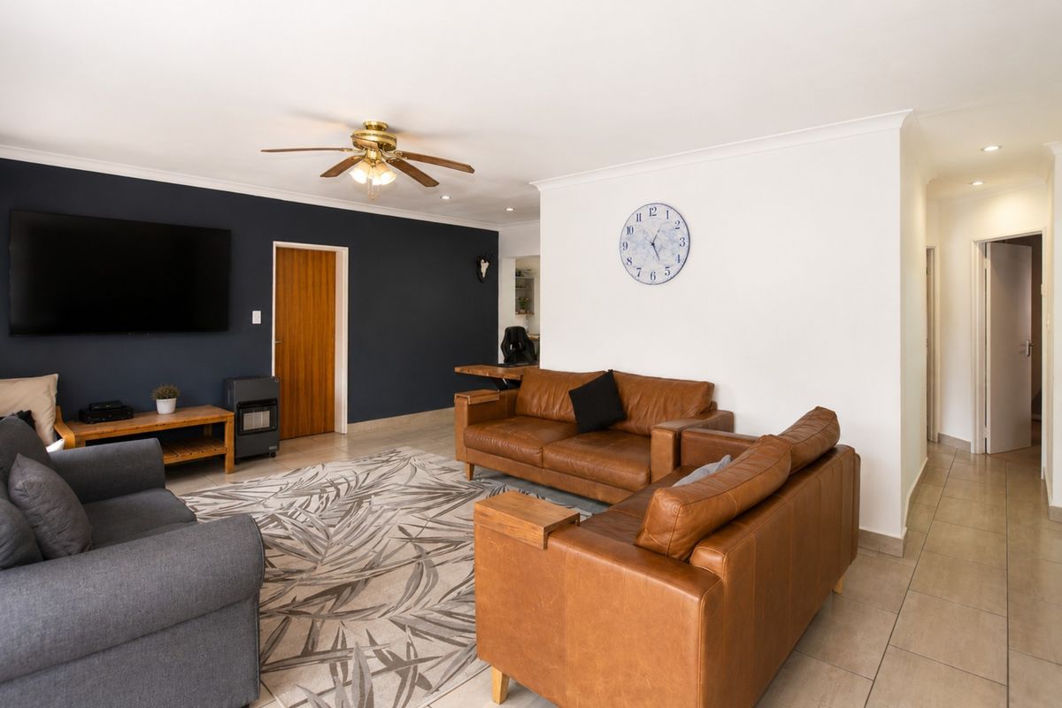 Spacious living room featuring tiled flooring, a ceiling fan, and a striking dark accent wall, providing a comfortable and well-maintained living space.