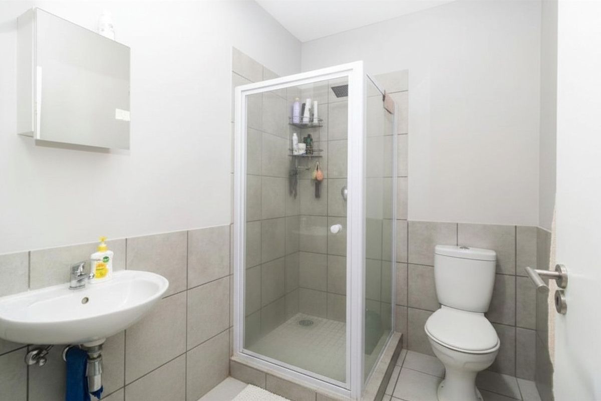 A functional bathroom featuring a glass-enclosed shower, a wall-mounted basin, and a standard toilet with neutral wall and floor tiling.