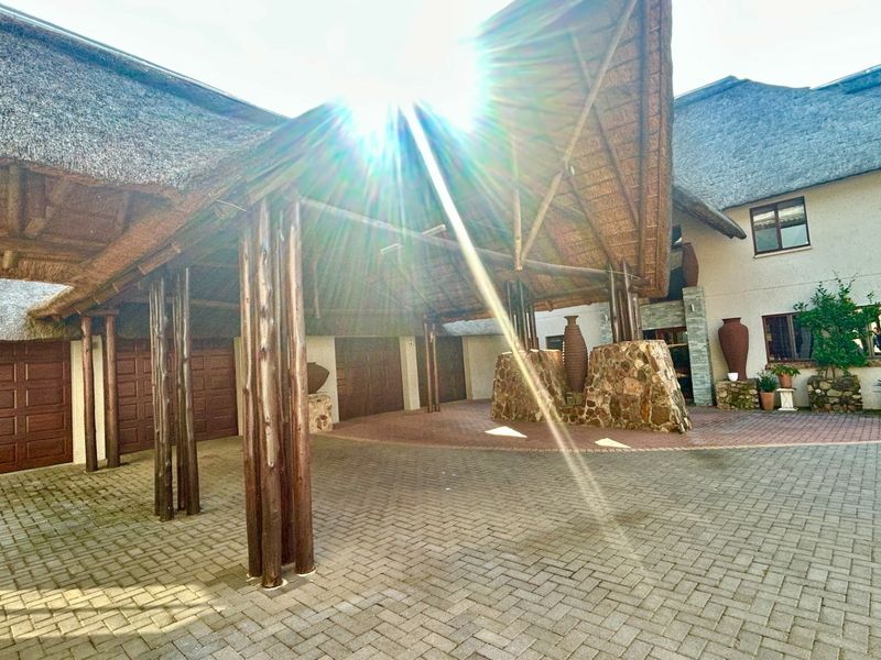 A spacious front entrance featuring a large thatched porte-cochère, paved driveway, and stone-clad architectural details, providing a grand and welcoming approach to the property.