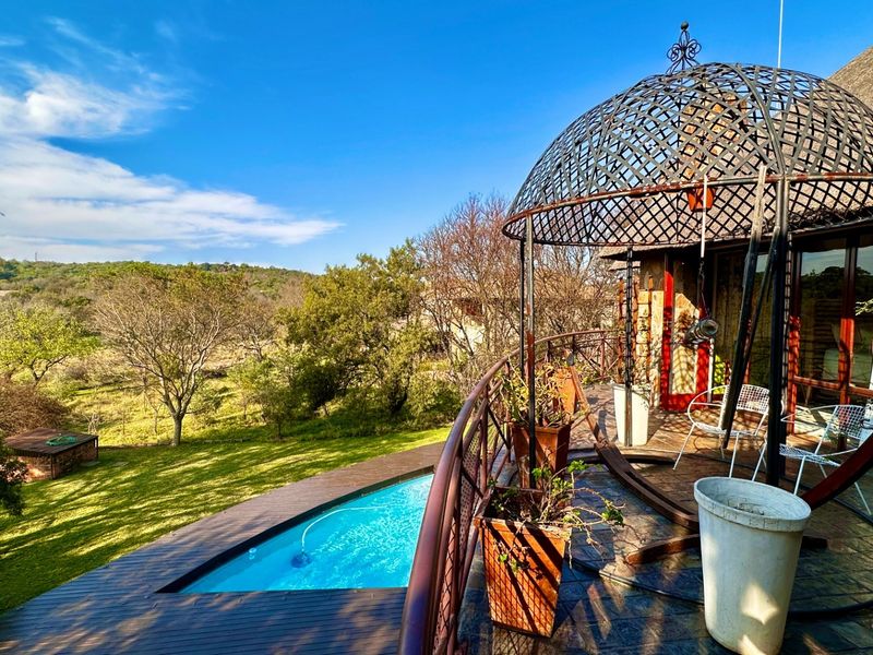 Outdoor pool area featuring wooden decking, a unique metal gazebo structure, and scenic views of the surrounding landscape.