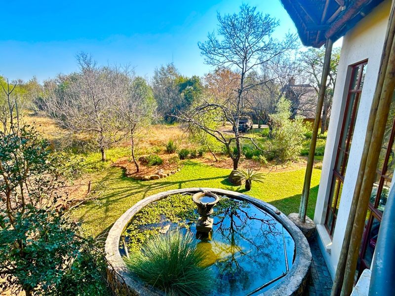 Elevated balcony view overlooking a landscaped garden featuring a circular stone water feature and mature trees.
