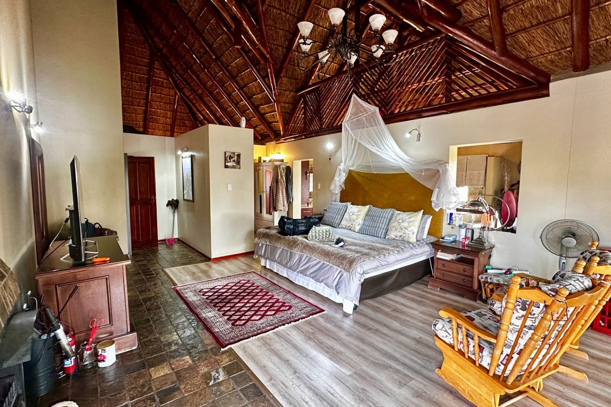Spacious bedroom featuring a high vaulted thatched ceiling with exposed timber rafters, a cozy fireplace, and a mix of stone and laminate flooring.