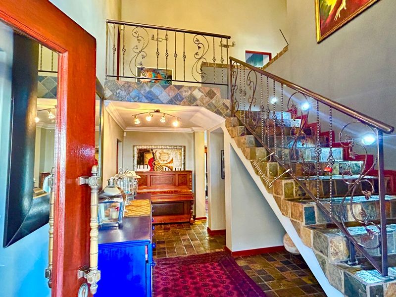 Grand entrance hall featuring a stone-tiled staircase with decorative wrought iron balustrades and high ceilings.