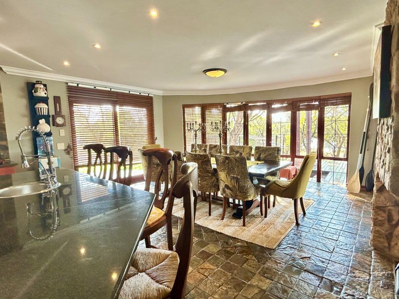 Spacious open-plan living and dining area featuring stone tile flooring, a prominent stone fireplace, and large folding glass doors leading to the outdoors.