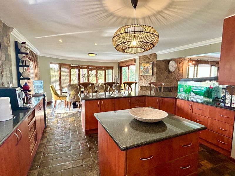 Spacious open-plan kitchen and dining area featuring granite countertops, warm wooden cabinetry, a central island, and a distinctive stone feature wall.