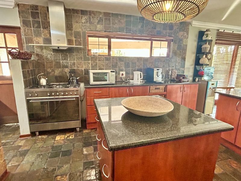 A functional kitchen featuring wooden cabinetry, granite countertops, a central island, and a stone tile backsplash with a stainless steel gas stove.