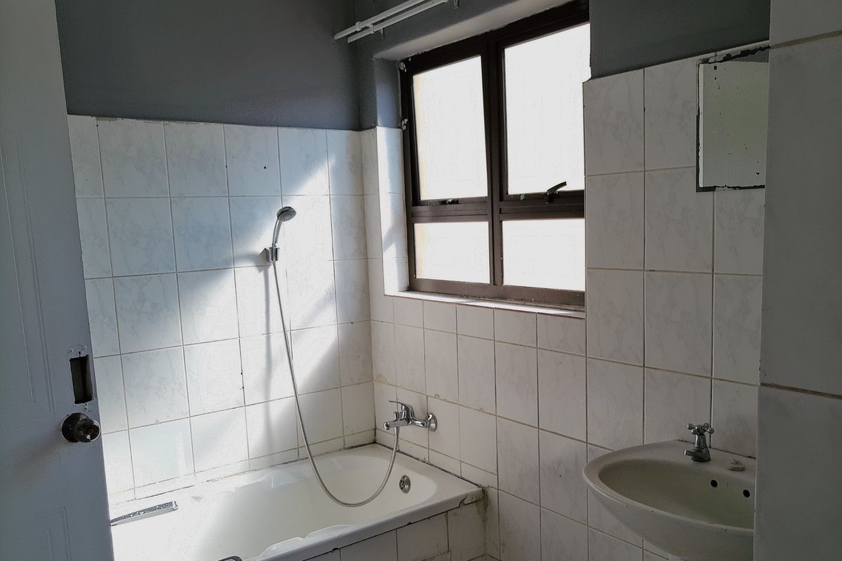 A dated bathroom featuring a bathtub with a handheld shower attachment, a pedestal basin, and tiled walls in need of maintenance.