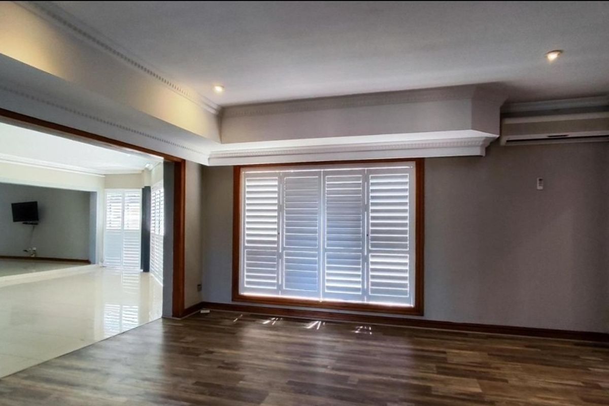 Spacious living area featuring wood-look flooring, recessed ceiling details with downlights, plantation shutters, and a wall-mounted air conditioning unit.