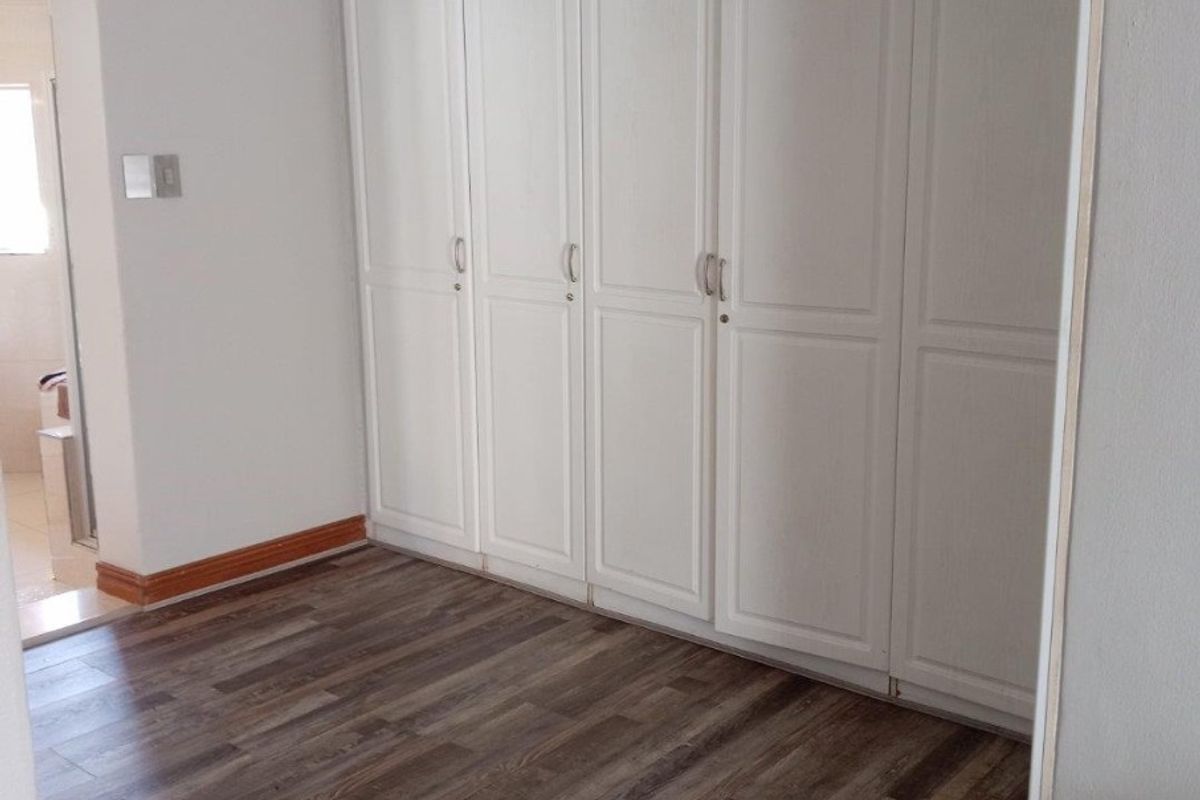 A bedroom featuring built-in white cabinetry, wood-look laminate flooring, and crown molding, with an adjacent view into a bathroom.