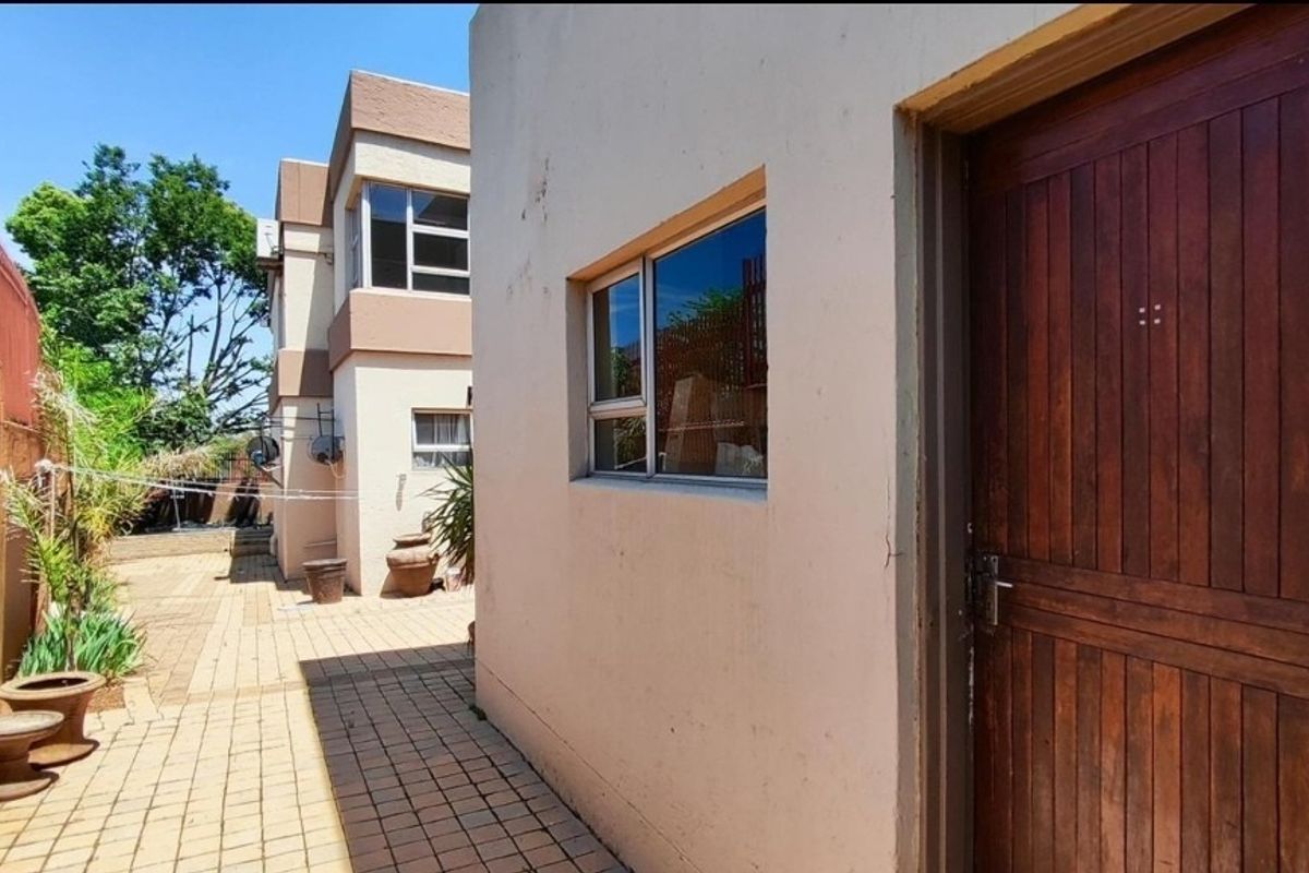 A view of the paved side exterior area featuring a wooden door, aluminum window frames, and a paved walkway leading to the rear of the property.