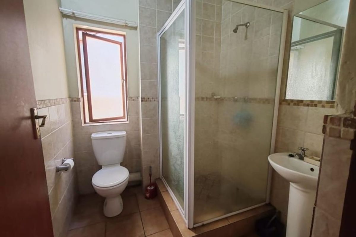 A functional bathroom featuring a corner shower enclosure, pedestal basin, and toilet with tiled walls and flooring.