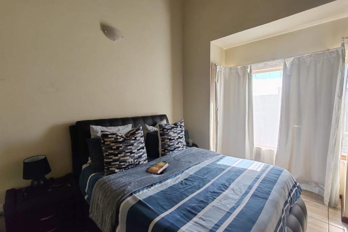 A bedroom featuring tiled flooring and a large window with curtains, providing natural light to the space.