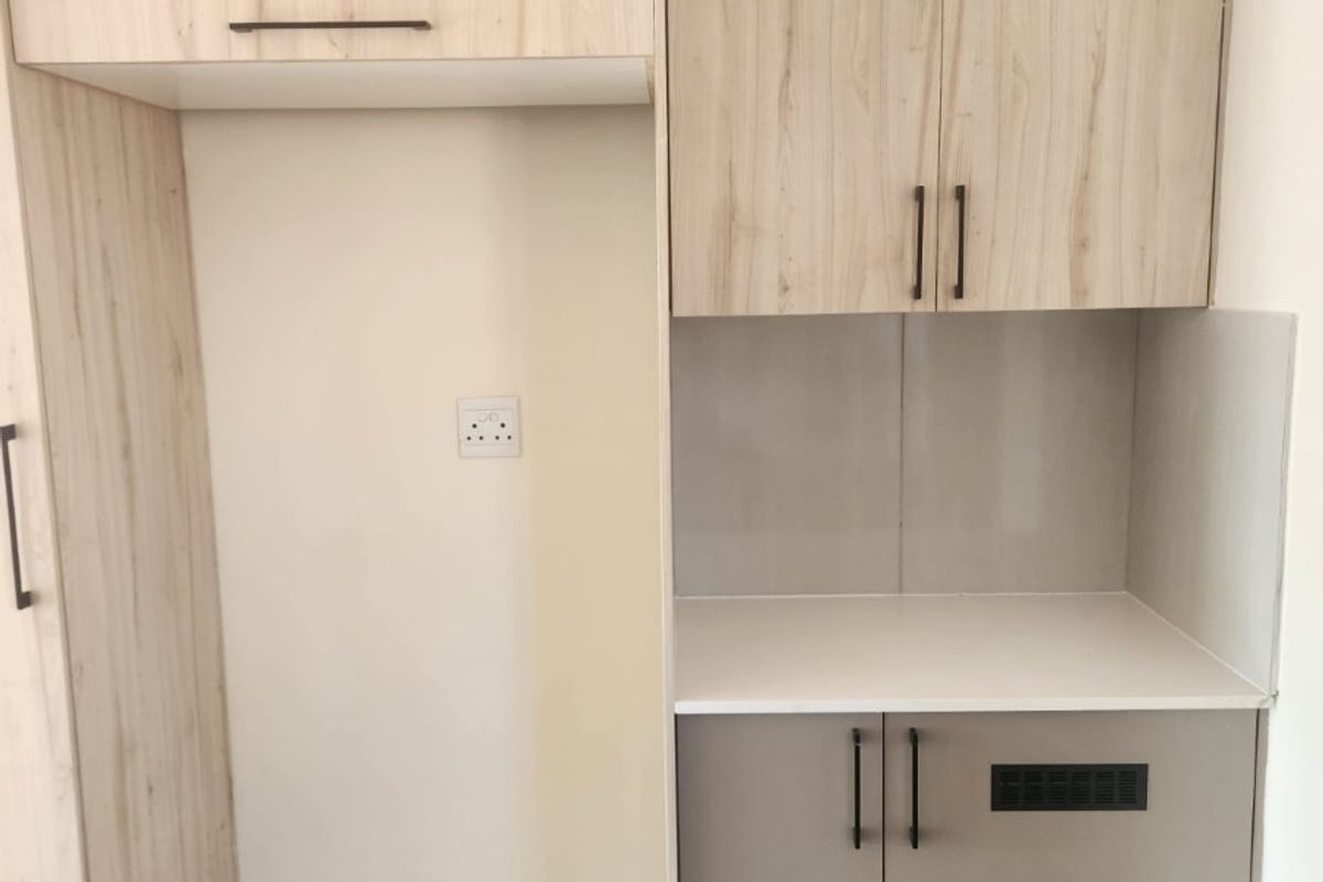 A modern kitchen utility area featuring light wood-grain cabinetry, a neutral countertop, and dedicated space for appliances with integrated ventilation.