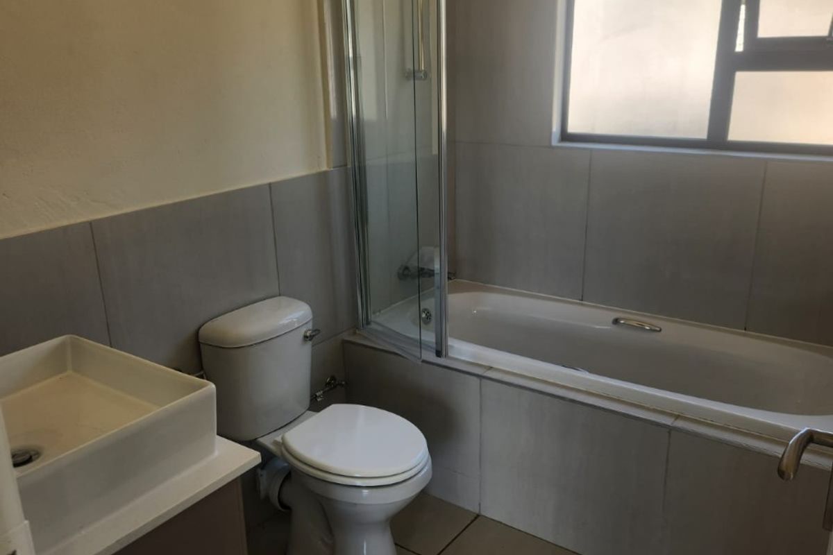 A functional bathroom featuring a built-in bathtub with a glass shower screen, a modern basin vanity, and a standard toilet.