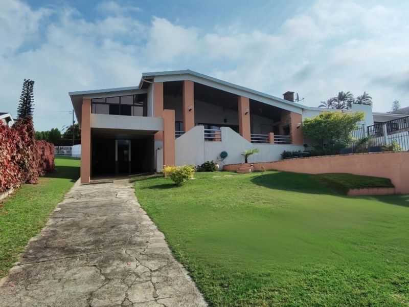 Front view of a residential house featuring a concrete driveway, covered patio area, and landscaped garden with a retaining wall.