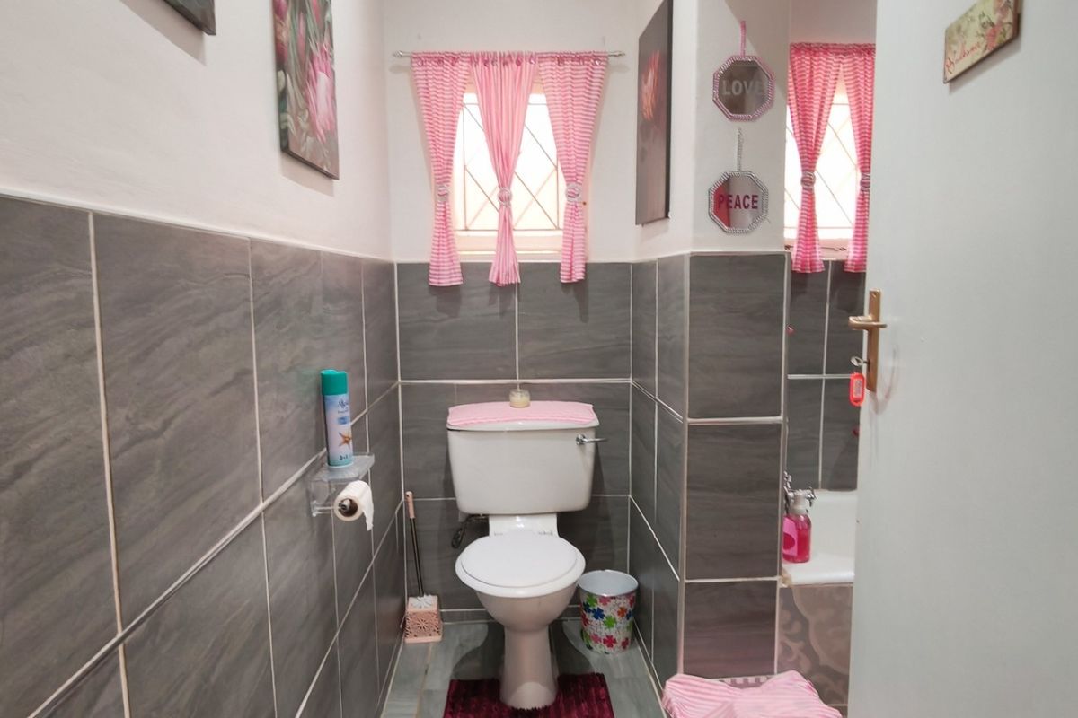 A compact bathroom featuring grey wall tiles, a standard toilet, and a bathtub with security bars on the window.
