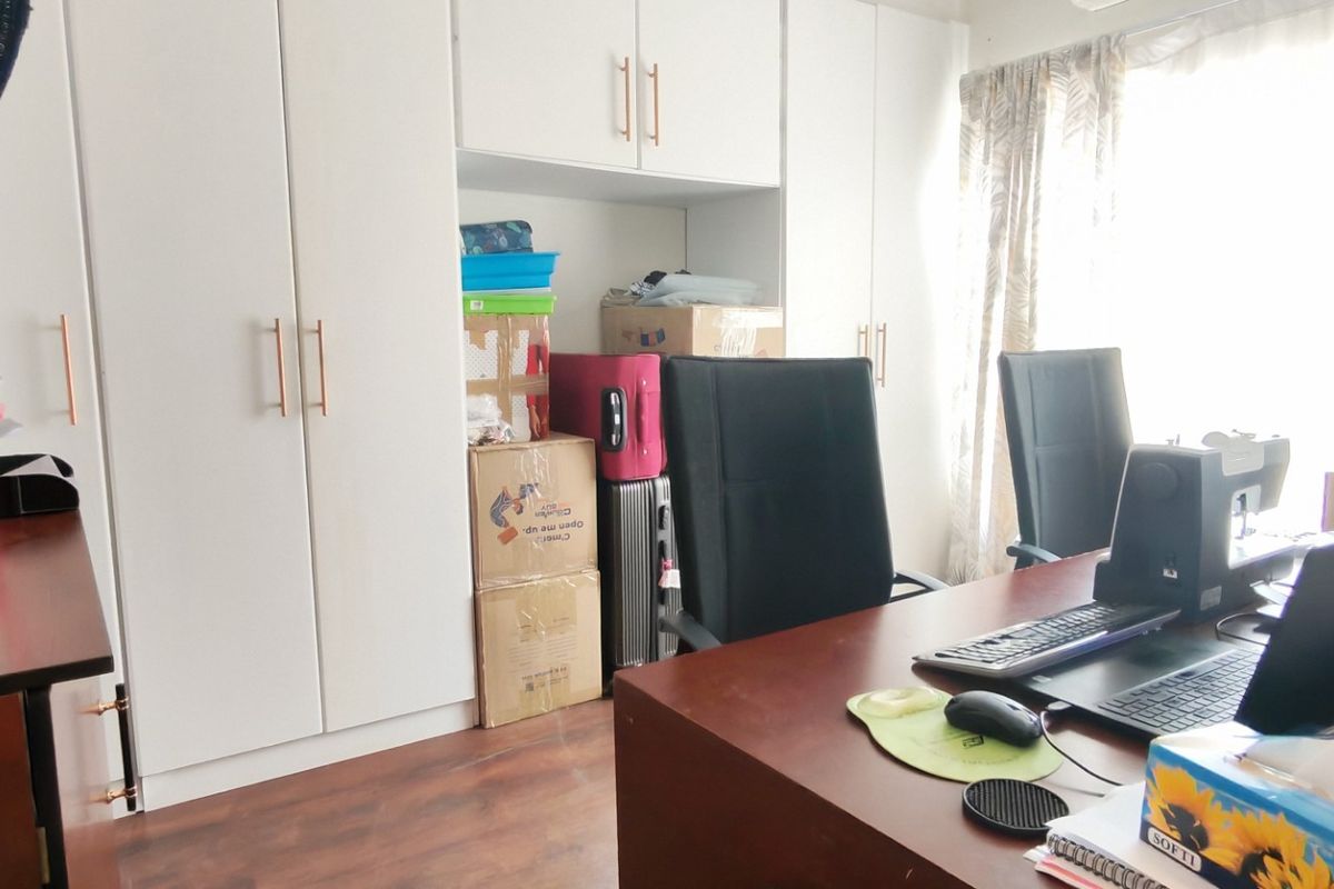A bedroom featuring extensive white built-in cupboards and laminate flooring, currently utilized as a home office space.