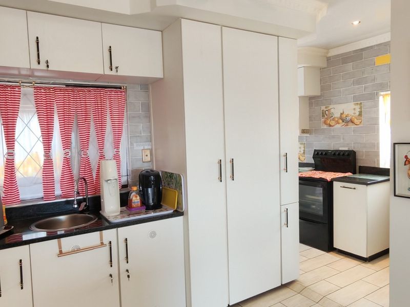 A functional kitchen featuring white cabinetry, granite countertops, tiled backsplash, and integrated cooking appliances with a view into the adjacent cooking area.