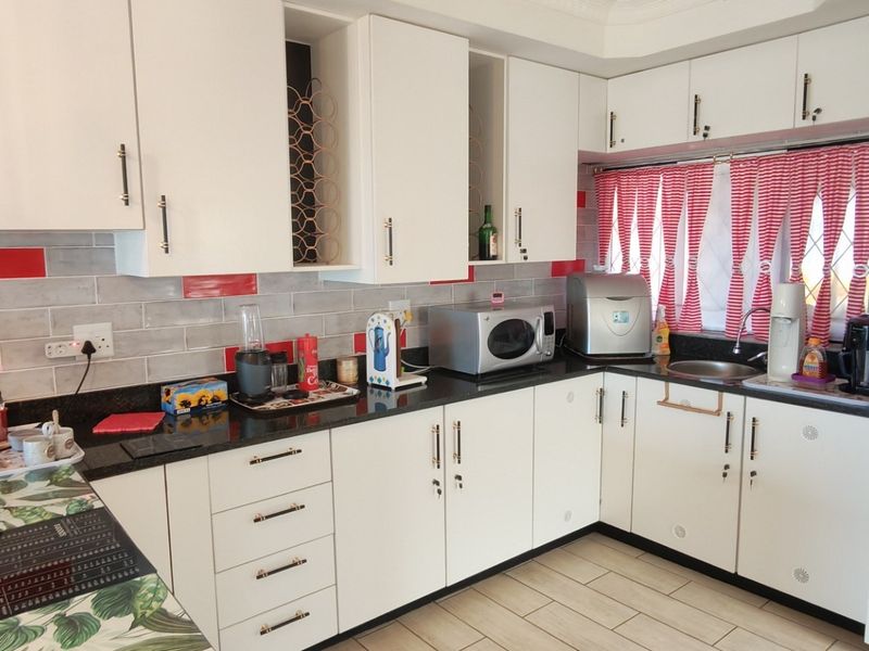 A functional kitchen featuring white cabinetry, contrasting black granite countertops, and a decorative subway tile backsplash with red accents.