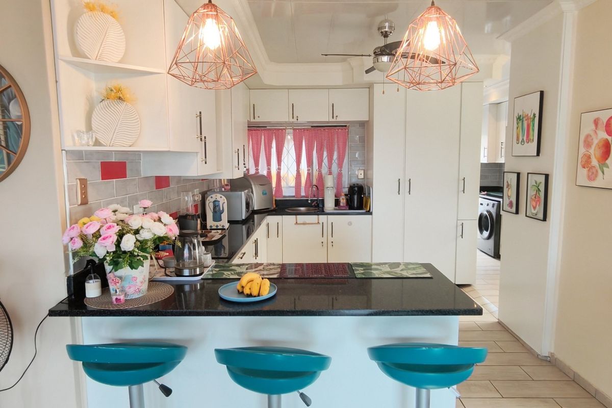 A functional kitchen featuring granite countertops, white cabinetry, a tiled backsplash, and modern pendant lighting, with an open-plan layout connecting to the living area.