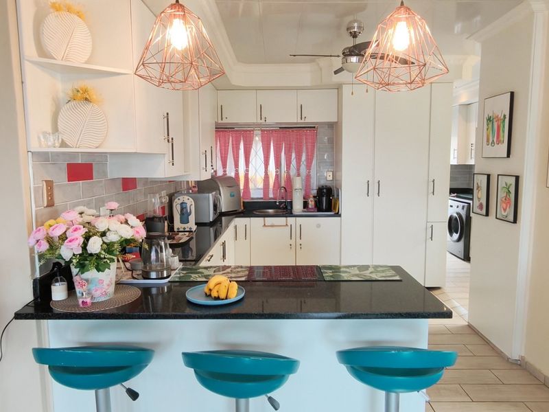 A functional kitchen featuring granite countertops, white cabinetry, a tiled backsplash, and modern pendant lighting, with an open-plan layout connecting to the living area.