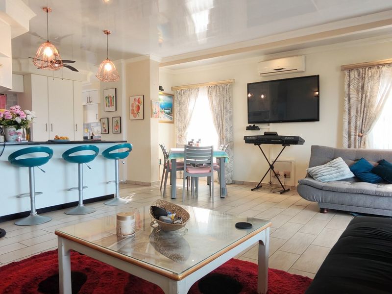 Spacious open-plan living and kitchen area featuring tiled flooring, a breakfast bar with pendant lighting, and a wall-mounted air conditioning unit.