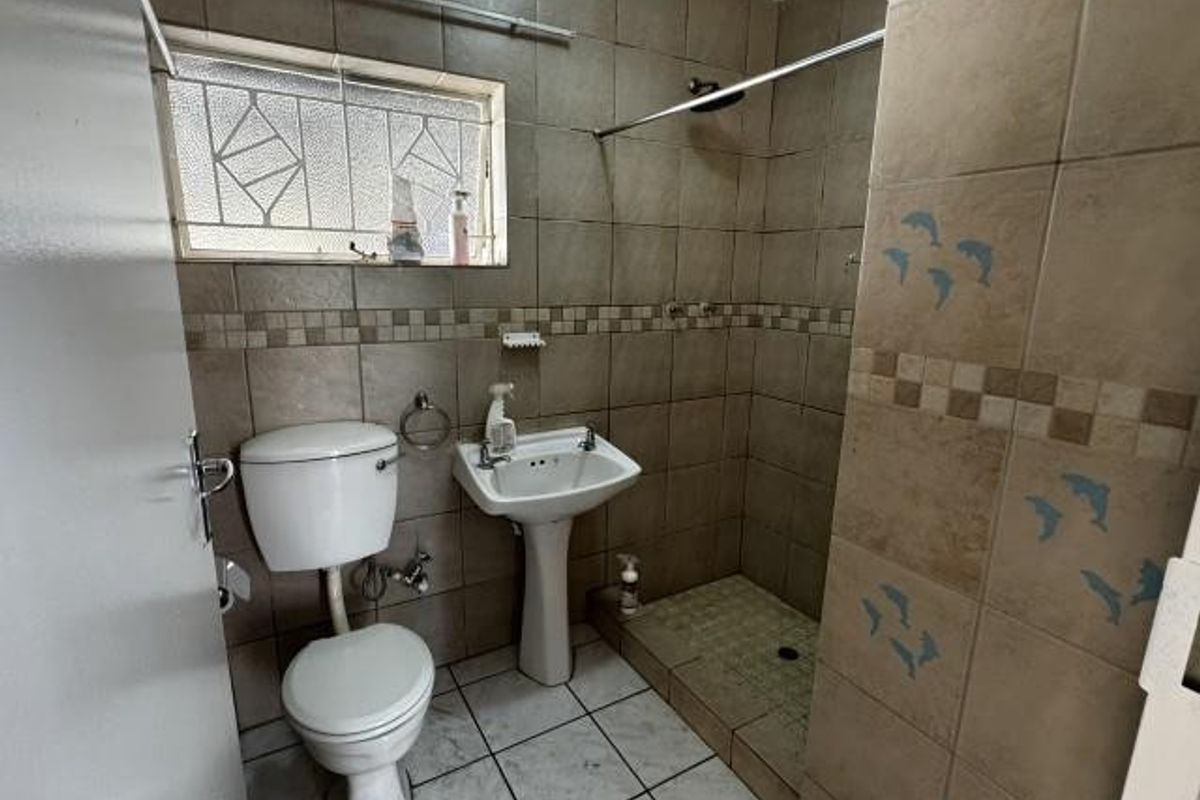 A compact bathroom featuring a pedestal basin, toilet, and a walk-in shower area with floor-to-ceiling tiled walls.