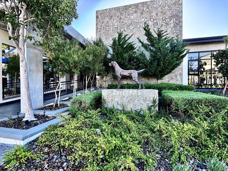 Exterior view of the apartment complex lifestyle centre, featuring stone cladding, landscaped garden beds, and a decorative sculpture.