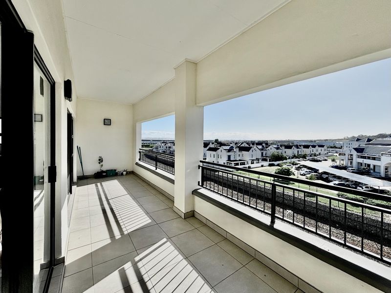 A spacious covered balcony featuring tiled flooring and metal railings, offering expansive views of the surrounding residential estate.