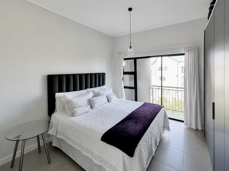 A bright bedroom featuring tiled flooring, built-in cupboards, and a sliding door leading to a private balcony.