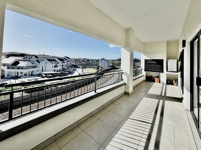 Spacious covered balcony featuring a built-in braai, tiled flooring, and metal railings, offering an elevated view of the surrounding residential complex.