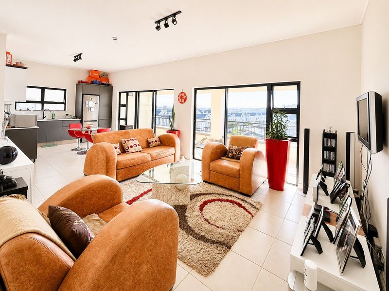 Open-plan living area featuring tiled flooring, modern kitchen cabinetry, and large sliding doors leading to a balcony with neighborhood views.