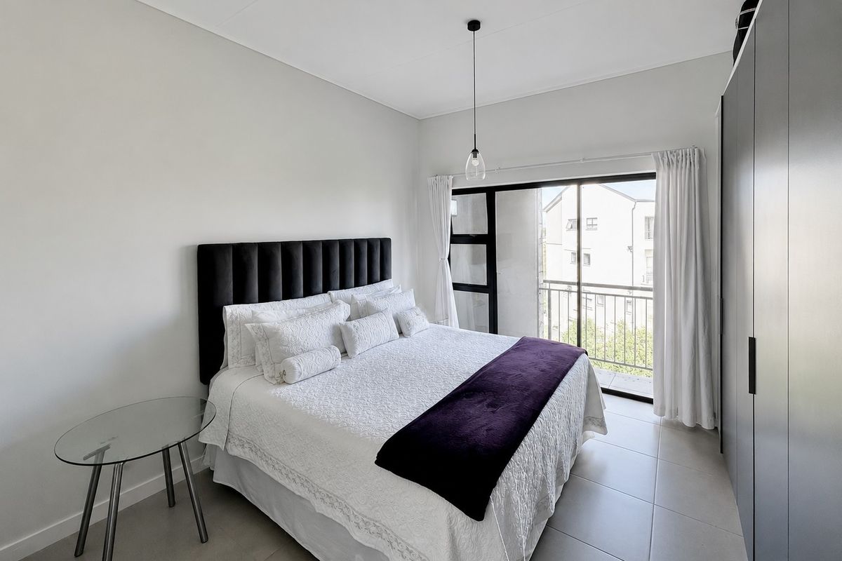 A bright bedroom featuring tiled flooring, built-in cupboards, and a sliding door leading to a private balcony.