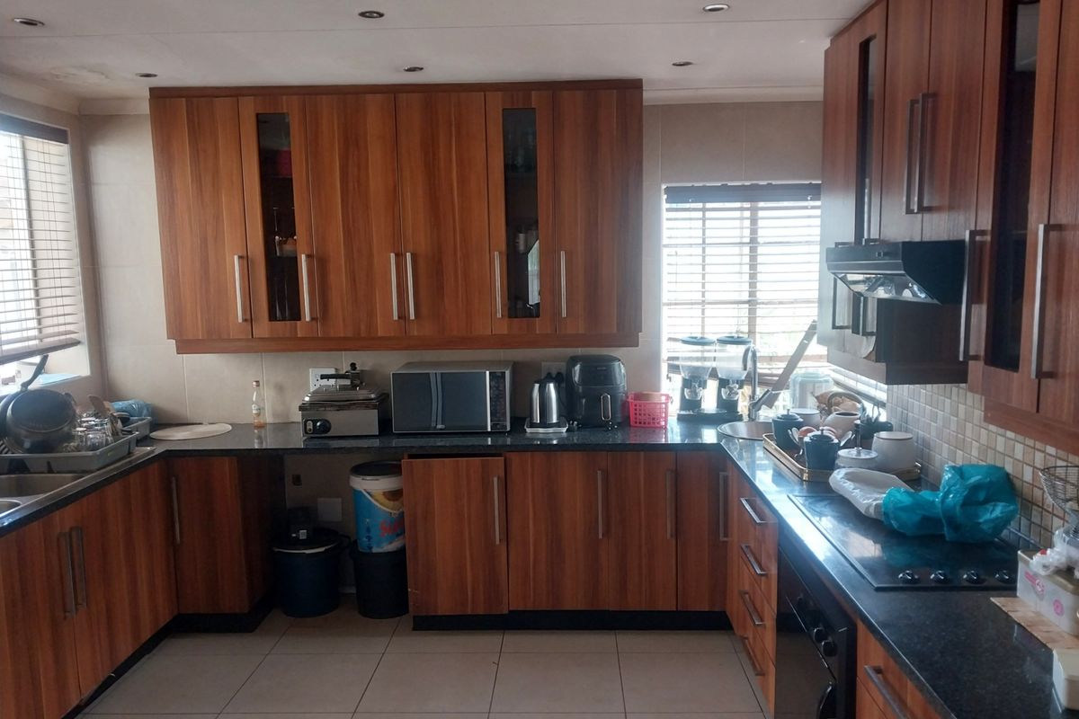 A functional kitchen featuring wood-grain cabinetry, dark granite countertops, tiled flooring, and integrated appliances including a hob and extractor fan.